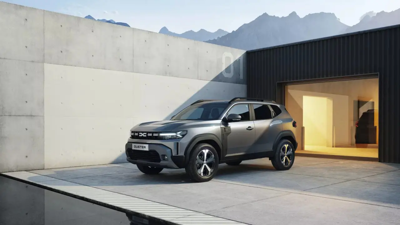 Treći Dacia Duster snimljen iz prednjeg ugla ispred moderne zgrade sa planinama u pozadini