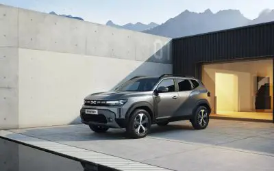Treći Dacia Duster snimljen iz prednjeg ugla ispred moderne zgrade sa planinama u pozadini