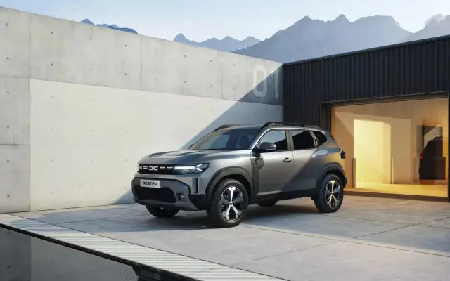 Treći Dacia Duster snimljen iz prednjeg ugla ispred moderne zgrade sa planinama u pozadini