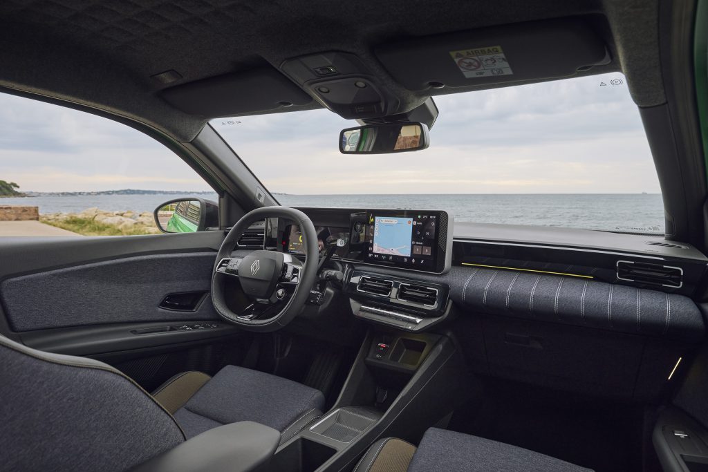 Enterijer Renault 5 E-Tech electric: digitalni instrument tabla, centralni ekran i volan, pogled sa suvozačke strane ka moru