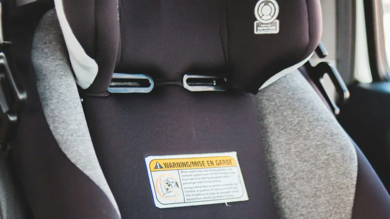 Detalj praznog dečijeg auto-sedišta u automobilu, sa kopčama pojasa i nalepnicom sa bezbednosnim uputstvom