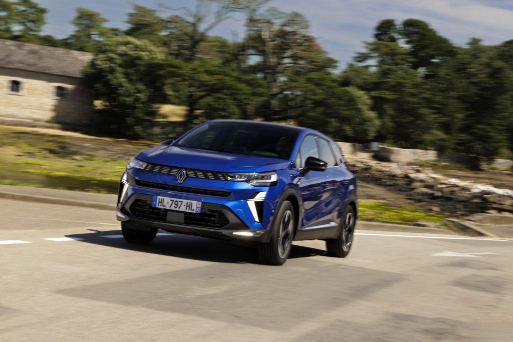 Plavi Renault Symbioz u vožnji, pogled na prednji desni ugao sa osvetljenom LED maskom i Renault dijamant znakom
