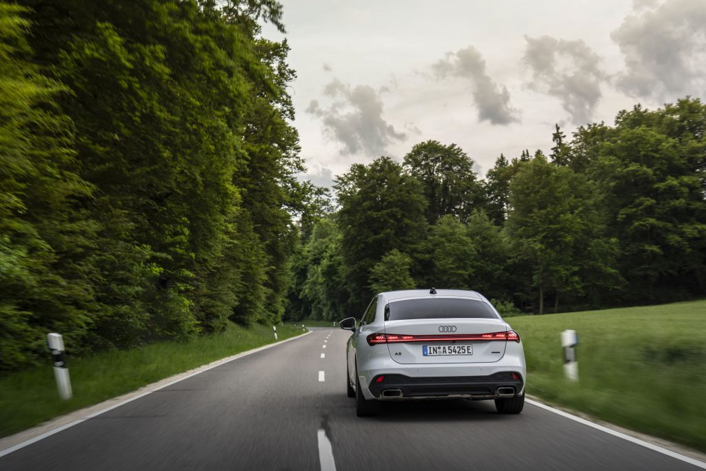 Audi A5 Sedan e-hybrid quattro u vožnji na seoskom putu, pogled pozadi sa upaljenim LED zadnjim svetlima
