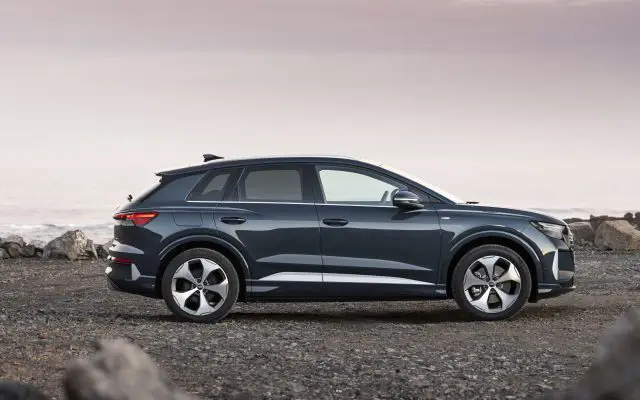 Audi Q4 e-tron u sivoplavoj boji, bočni profil, parkiran na kamenitoj obali u sumrak