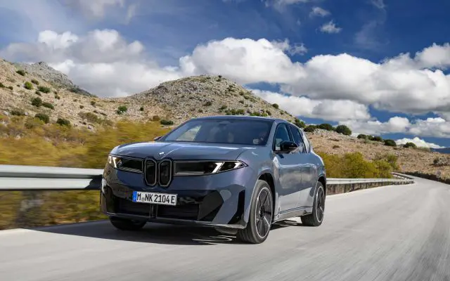 BMW iX3 50 xDrive u voznji na planinskom putu, pogled spreda i sa strane