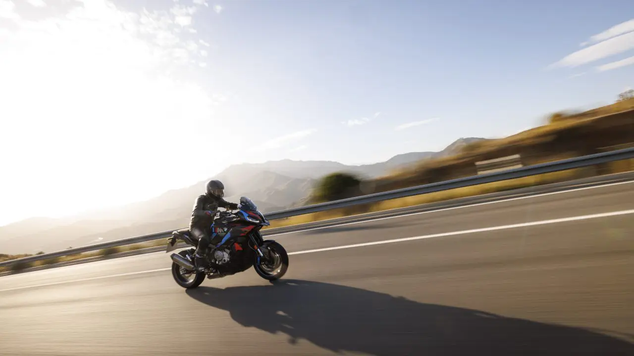 BMW M 1000 XR, bočni ugao u pokretu na planinskom putu, M bojama (crveno-plavo-ljubičasto) na crnoj podlozi