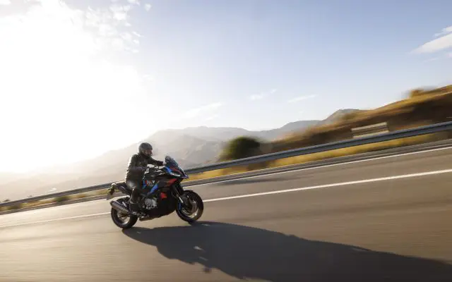 BMW M 1000 XR, bočni ugao u pokretu na planinskom putu, M bojama (crveno-plavo-ljubičasto) na crnoj podlozi