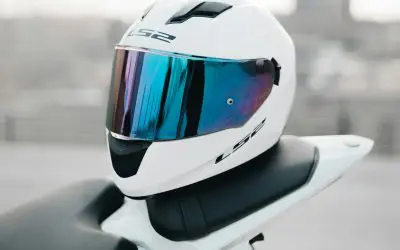 Bela integralna moto kaciga sa reflektujućim vizirom, krupni plan, motocikl i grad u pozadini