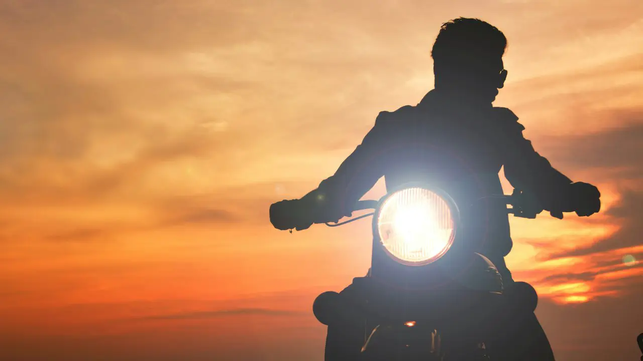 Silueta motocikliste u vožnji pri zalasku sunca, pogled sa prednjim farom